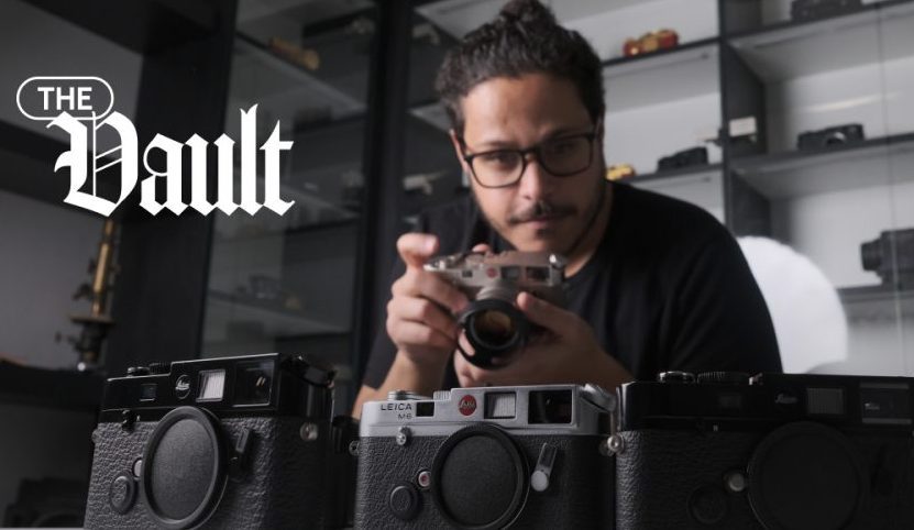 Photo of John L. holding a Leica M6, pointed at a table full of other rare Leica M6 cameras, with the Vault logo lockup in the top left corner